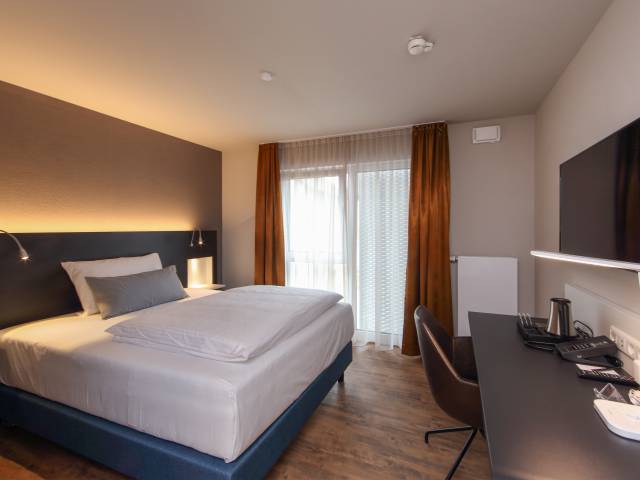 Business Zimmer mit Bett, Tisch und TV im Estilo Design & Lifestyle Hotel Aalen