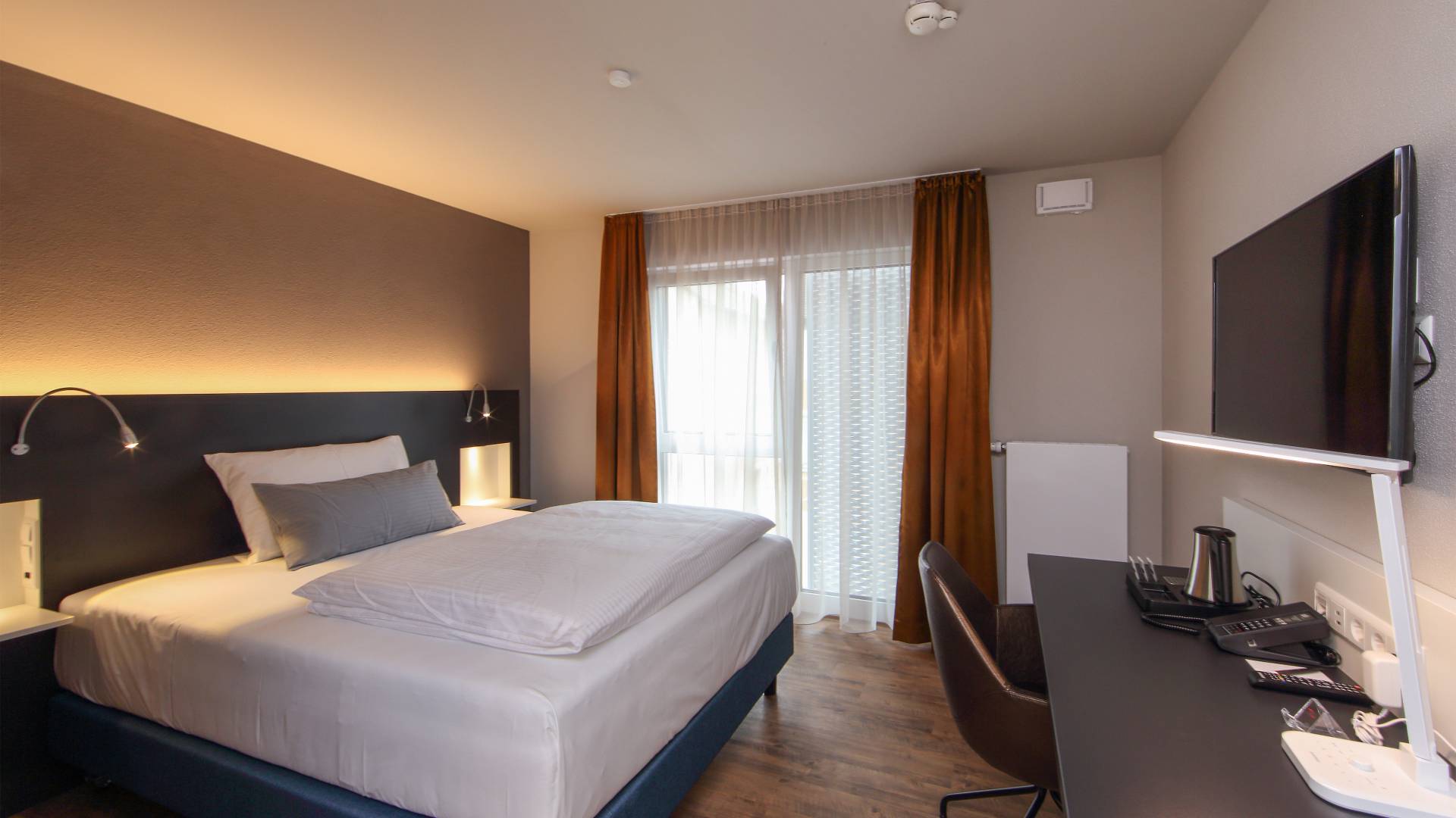 Business Zimmer mit Bett, Tisch und TV im Estilo Design & Lifestyle Hotel Aalen